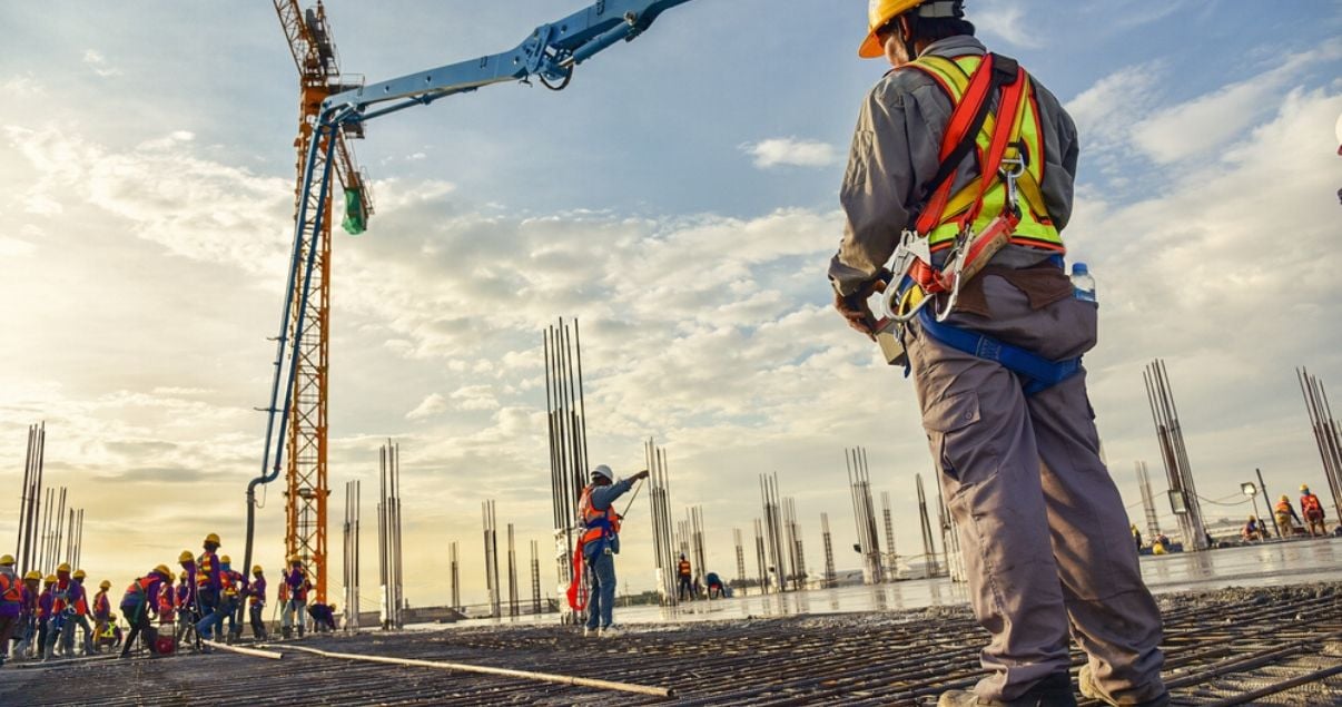 Trabajadores en una construcción de apartamentos en pozo controlan una bomba de hormigón con una grúa
